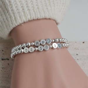 May include: Two silver bead bracelets with silver charms. The charms spell out "M♡Z 10 25 08".