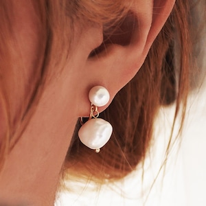 Puede incluir: Un par de pendientes de perlas con un diseño de gota. Los pendientes están hechos de oro y presentan dos perlas blancas.