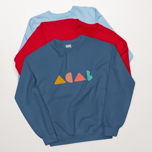 K&ouml;nnte beinhalten: Drei &uuml;bereinander gelegte Sweatshirts in Blau, Rot und Hellblau. Das vorderste blaue Sweatshirt zeigt den Text "ACAB" in farbenfrohen geometrischen Formen. Der Text besteht aus einem gelben Dreieck, einem pfirsichfarbenen Halbkreis, einem korallenfarbenen Dreieck und einem gr&uuml;nen Halbkreis.
