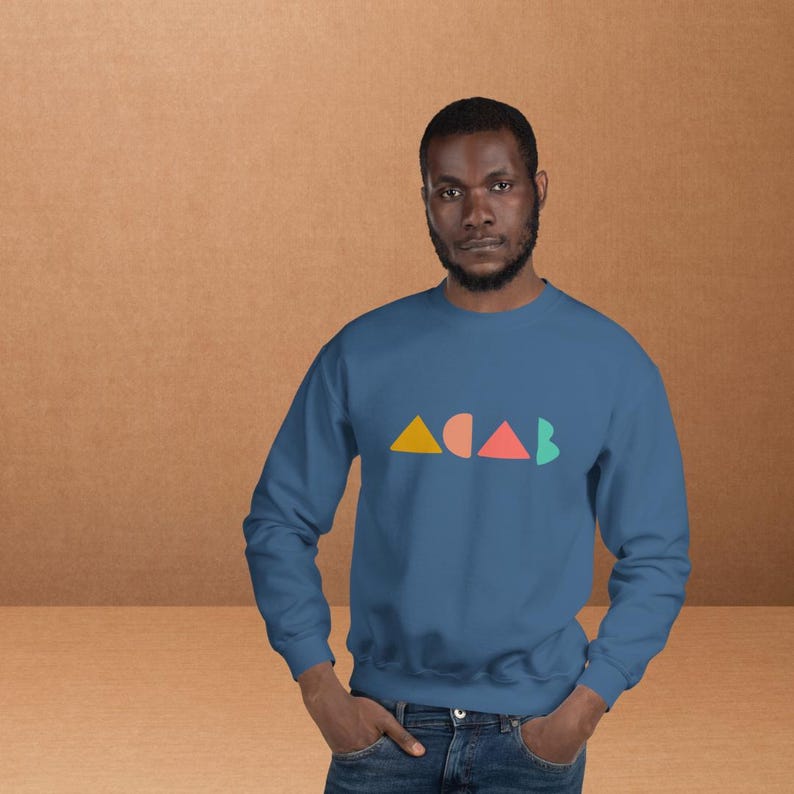 K&ouml;nnte beinhalten: Ein blaues Sweatshirt mit den Buchstaben "ACAB" in bunten geometrischen Formen. Die Buchstaben sind gelb, korallenfarben und gr&uuml;n. Das Sweatshirt ist einfarbig und hat lange &Auml;rmel.