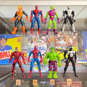 May include: Collection of action figures featuring various comic book characters, including Spider-Man, Green Goblin, and Hulk. The figures are displayed in front of baseball card boxes. The figures are approximately 6 inches tall.