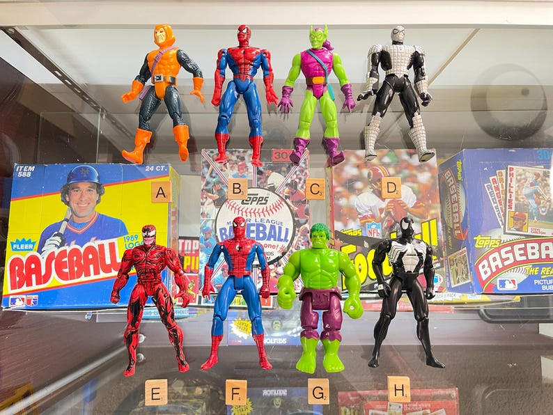 May include: Collection of action figures featuring various comic book characters, including Spider-Man, Green Goblin, and Hulk. The figures are displayed in front of baseball card boxes. The figures are approximately 6 inches tall.