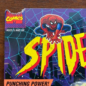 May include: A vintage Marvel Comics action figure packaging featuring Spider-Man in a red and blue suit. The packaging has a yellow and red "SPIDER" logo and the text "Punching Power!"  The packaging is for ages 5 and up.