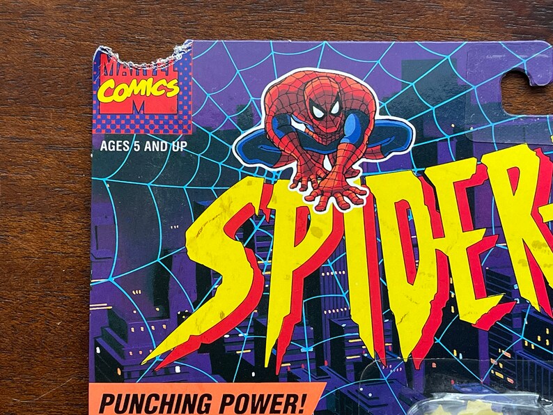 May include: A vintage Marvel Comics action figure packaging featuring Spider-Man in a red and blue suit. The packaging has a yellow and red "SPIDER" logo and the text "Punching Power!"  The packaging is for ages 5 and up.