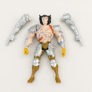 May include: A Wolverine action figure with black hair, a scarred chest, and silver armor plating on the shoulders, arms, and legs. The figure wears gold-colored boots and gloves, and is accompanied by two detachable silver mechanical arm attachments.