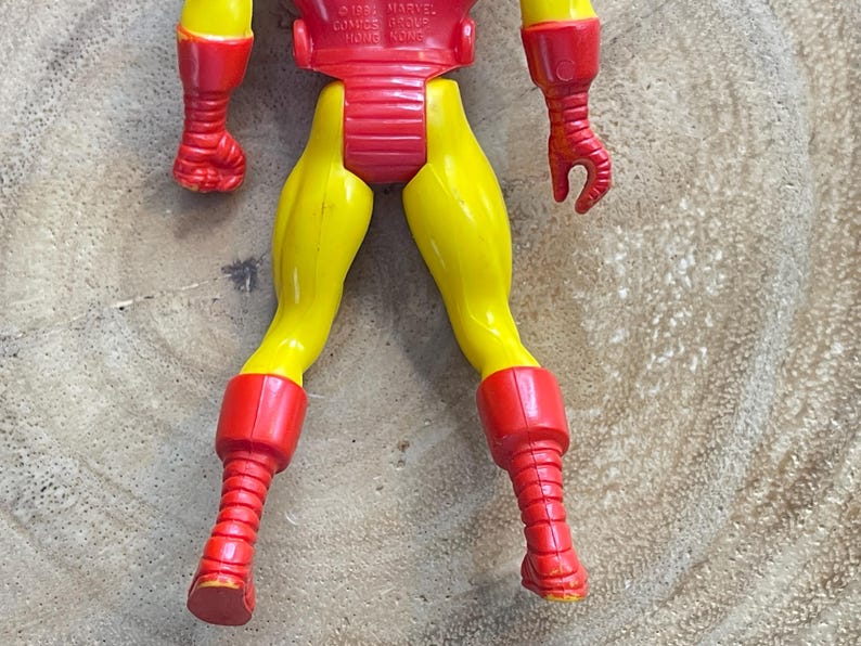 May include: A vintage Iron Man action figure, featuring a red and yellow color scheme. The figure's legs are yellow, with red boots and a red torso. The arms are red. The figure is made of plastic and shows signs of wear.