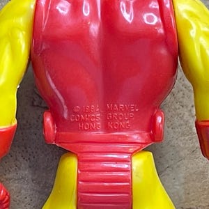 May include: A close-up of a vintage Iron Man action figure. The figure is primarily red and yellow, with the text "&copy; 1993 MARVEL COMICS GROUP HONG KONG" imprinted on the back. The figure's arms and legs are yellow, and the torso is red.