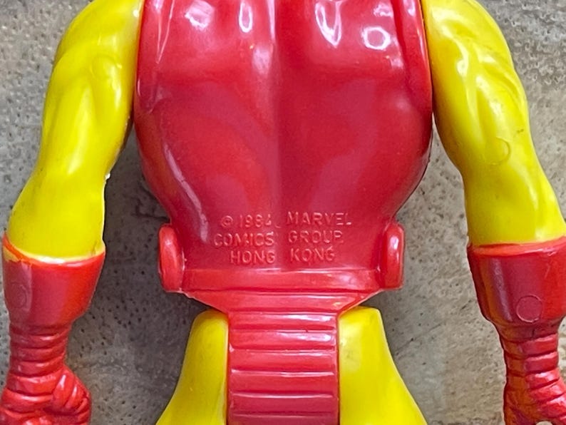 May include: A close-up of a vintage Iron Man action figure. The figure is primarily red and yellow, with the text "&copy; 1993 MARVEL COMICS GROUP HONG KONG" imprinted on the back. The figure's arms and legs are yellow, and the torso is red.