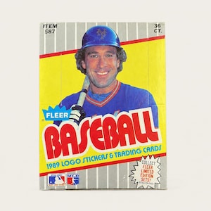 May include: A 1989 Fleer baseball trading card box featuring a player in a blue jersey and helmet holding a bat. The yellow and grey box displays the text FLEER BASEBALL, 1989 LOGO STICKERS & TRADING CARDS, ITEM 587, 36 CT., and COLLECT FLEER LIMITED EDITION SETS.