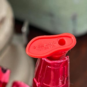 Pode incluir: Close-up de um p&eacute; de brinquedo de pl&aacute;stico vermelho com um buraco. O texto "&copy; 1995 MARVEL" &eacute; vis&iacute;vel. O brinquedo faz parte de uma figura maior, com um torso vermelho e outras partes vis&iacute;veis no fundo.