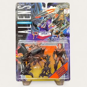 May include: An Aliens Space Marine Atax action figure in original packaging. The set includes a brown, multi-legged vehicle with a black cockpit and a Space Marine figure with red hair. The card features the Aliens logo and product text.
