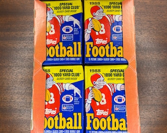 May include: Four unopened boxes of 1988 Topps Football cards. Each box features a red, white, and blue design with the text "Special "1000 Yard Club" Glossy Card Inside" and a picture of a football player wearing a red jersey with the number 18.