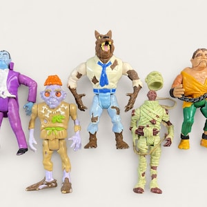 May include: A set of five plastic monster action figures including a vampire in a purple suit, a small creature with orange hair, a werewolf in a blue shirt and tie, a mummy with a detached head piece, and a figure holding a black chain.