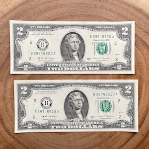 May include: Two $2 bills with the portrait of Thomas Jefferson on them. The serial numbers are B 39745520 A and B 39745519 A.