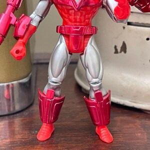 Pode incluir: Figura de a&ccedil;&atilde;o vermelha e prateada com juntas articuladas. A figura tem tronco, bra&ccedil;os e pernas vermelhas, com detalhes prateados nas pernas e bra&ccedil;os. A figura est&aacute; em pose com os bra&ccedil;os estendidos.