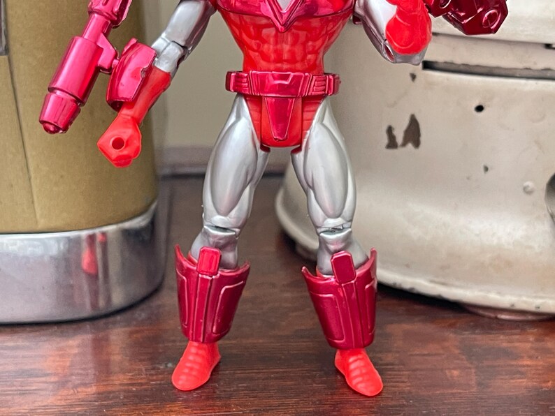 Pode incluir: Figura de a&ccedil;&atilde;o vermelha e prateada com juntas articuladas. A figura tem tronco, bra&ccedil;os e pernas vermelhas, com detalhes prateados nas pernas e bra&ccedil;os. A figura est&aacute; em pose com os bra&ccedil;os estendidos.