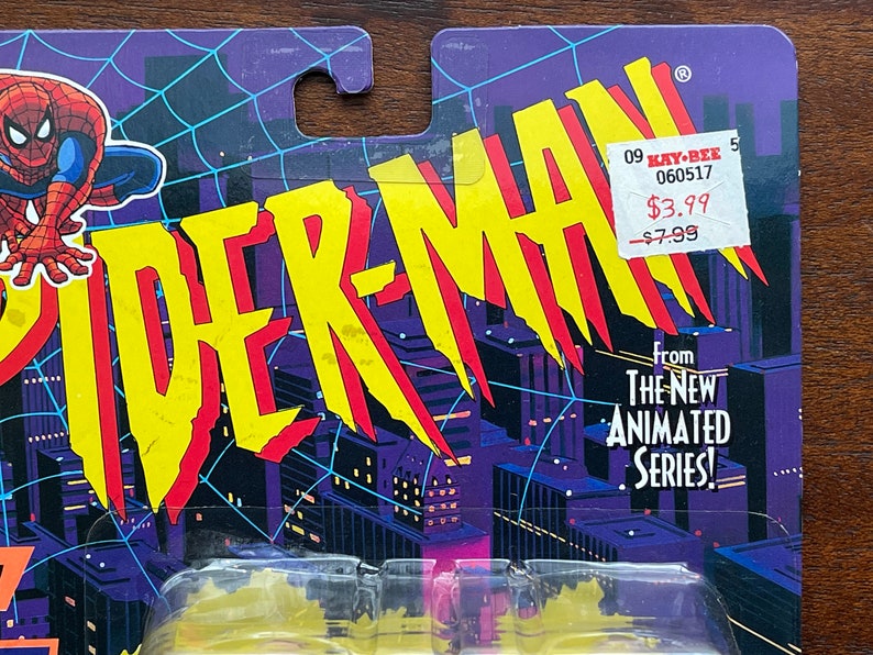 May include: A vintage action figure card featuring Spider-Man from the animated series. The card is yellow, red, and blue with a cityscape background. The price tag reads "$3.99" and "-$7.99".