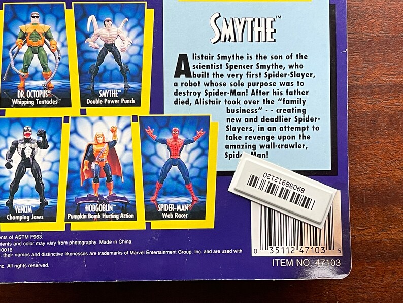 May include: A close-up of a Spider-Man action figure packaging featuring a variety of Spider-Man villains, including Dr. Octopus, Venom, Hobgoblin, and Smythe. The packaging is blue and yellow with a white background. The text on the packaging reads "Smythe" and "Item No. 47103".