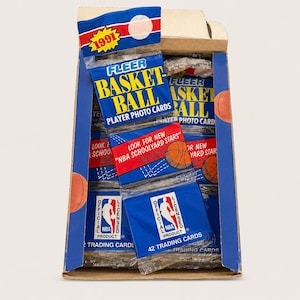 May include: A cardboard display box containing multiple 1991 Fleer basketball player photo card packs. Each pack features blue, red, and white branding with the text Fleer Basketball Player Photo Cards, Look for New NBA Schoolyard Stars, and Official NBA Product.