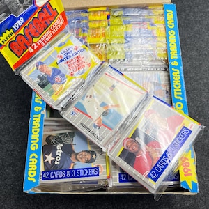 May include: A box of 1989 Fleer Baseball trading cards and stickers. The box is blue and yellow, with packs of cards visible. Each pack contains 42 cards and 3 stickers. The packs are sealed in clear plastic.
