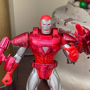 Pode incluir: Uma figura de a&ccedil;&atilde;o do Homem de Ferro vermelha e prateada. A figura tem um capacete, peito e bra&ccedil;os vermelhos, com detalhes prateados nas pernas e articula&ccedil;&otilde;es. A figura posa com uma m&atilde;o levantada e o outro bra&ccedil;o estendido.