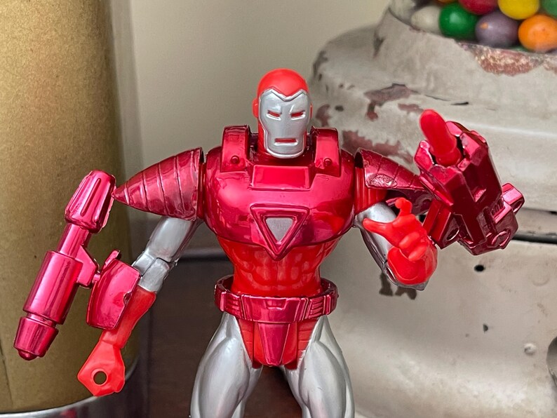 Pode incluir: Uma figura de a&ccedil;&atilde;o do Homem de Ferro vermelha e prateada. A figura tem um capacete, peito e bra&ccedil;os vermelhos, com detalhes prateados nas pernas e articula&ccedil;&otilde;es. A figura posa com uma m&atilde;o levantada e o outro bra&ccedil;o estendido.