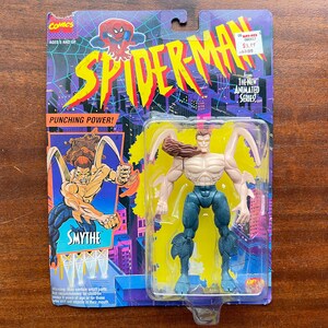 May include: A plastic action figure of the Spider-Man villain, Smythe, from the 1990s animated series. The figure is in a clear plastic blister pack with a blue, yellow, and purple background. The packaging features the Spider-Man logo and the text "Punching Power!" and "The Next Animated Series".