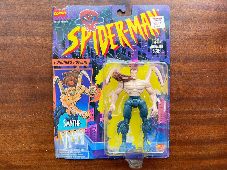 May include: A plastic action figure of the Spider-Man villain, Smythe, from the 1990s animated series. The figure is in a clear plastic blister pack with a blue, yellow, and purple background. The packaging features the Spider-Man logo and the text "Punching Power!" and "The Next Animated Series".
