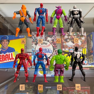 May include: Collection of vintage action figures, including Spider-Man, Hobgoblin, and Venom. The figures are posed in front of baseball card boxes and a baseball card. The figures are various colors.