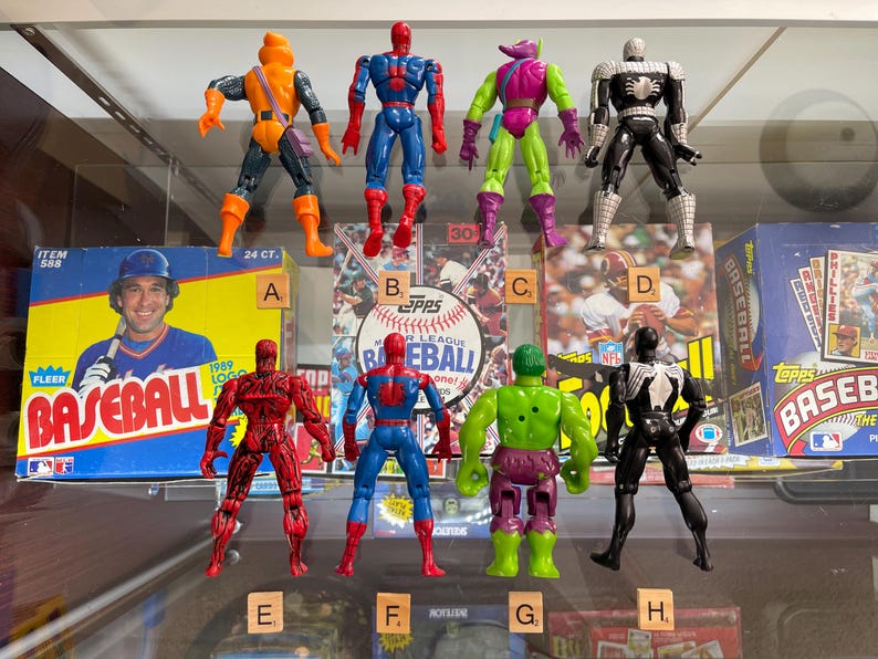 May include: Collection of vintage action figures, including Spider-Man, Hobgoblin, and Venom. The figures are posed in front of baseball card boxes and a baseball card. The figures are various colors.