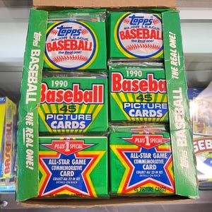 May include: A collection of vintage 1990 Topps Major League Baseball card packs. The packs are green, red, and yellow, with the Topps logo and baseball imagery. The box also includes All-Star Game commemorative cards.