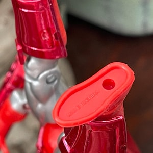 Pode incluir: Close-up de uma figura de a&ccedil;&atilde;o vermelha e prateada. O p&eacute; da figura &eacute; vermelho com um buraco e o texto "MADE IN CHINA". A perna e outras partes da figura s&atilde;o vis&iacute;veis.