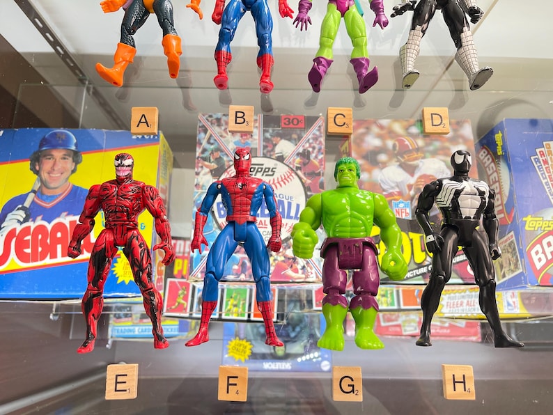 May include: A collection of action figures featuring comic book characters. The figures include Spider-Man, Hulk, Venom, and Carnage. The figures are displayed in front of baseball card boxes and a baseball-themed box.