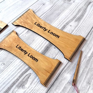 May include: Two wooden weaving looms with the text "Liberty Loom" printed on them. A small wooden comb and a needle with a pink thread are also included.