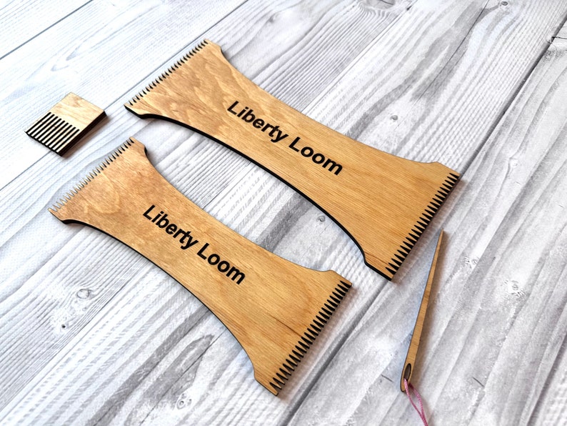 May include: Two wooden weaving looms with the text "Liberty Loom" printed on them. A small wooden comb and a needle with a pink thread are also included.