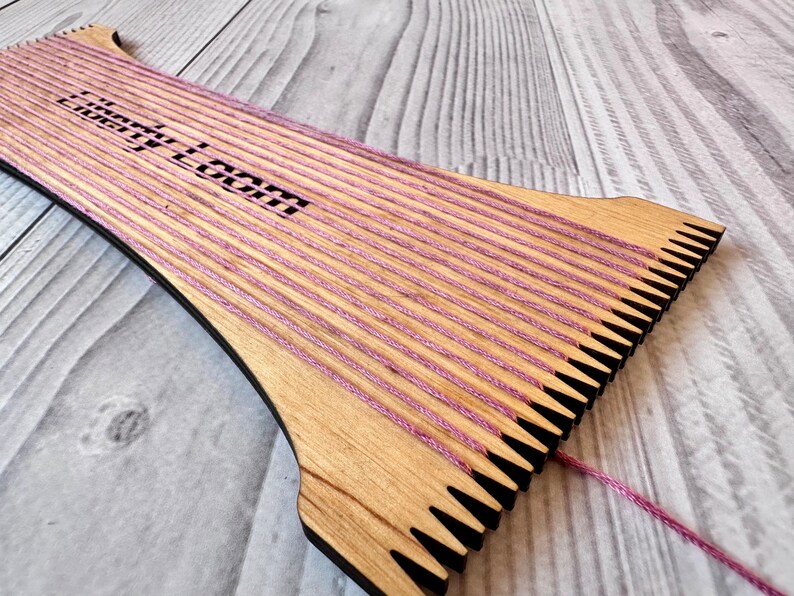 May include: A wooden loom with pink yarn strung across it. The loom is labeled "Little Loom".