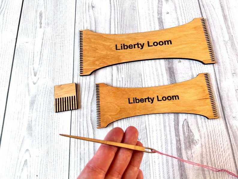 May include: Two wooden looms with the text "Liberty Loom" printed on them. A small wooden comb and a wooden needle with pink yarn are also included.