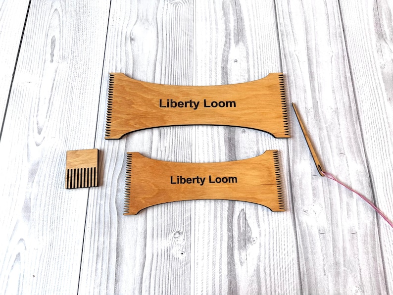 May include: Two wooden knitting looms with the text "Liberty Loom" printed on them. A small wooden comb and a pink yarn needle are also included.