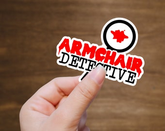 May include: White sticker with red and black text that reads "Armchair Detective" with a black and white magnifying glass icon with a red splatter inside.