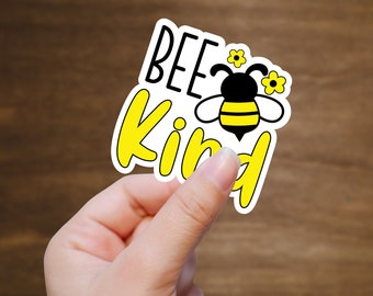 May include: A white sticker with the text "Bee Kind" in yellow and black lettering. A cartoon bee with black and yellow stripes is in the center of the sticker.