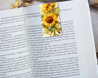May include: A watercolor painting of sunflowers with green leaves on a white background. The sunflowers are in various stages of bloom, with some fully open and others still in bud. The painting is framed by a book page with text in Polish.