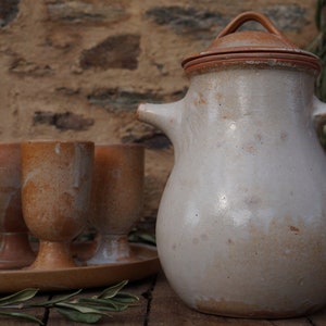 Peut inclure: Un ensemble de six tasses en céramique et un pichet en céramique avec un couvercle, tous dans des tons de brun et de blanc. Les tasses sont sur un plateau et le pichet est sur une surface en bois.