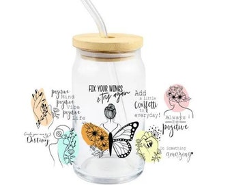 May include: A glass jar with a wooden lid and a straw. The jar features a butterfly design and inspirational quotes, such as "Fix your wings & try again", "Add a little confetti to everyday!" and "Always be positive".
