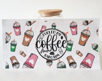 May include: A white wrap featuring a pattern of coffee drinks in pink, brown, and green, with a bamboo lid. The wrap has the text "Fueled by Coffee and Sarcasm" in a black circle.