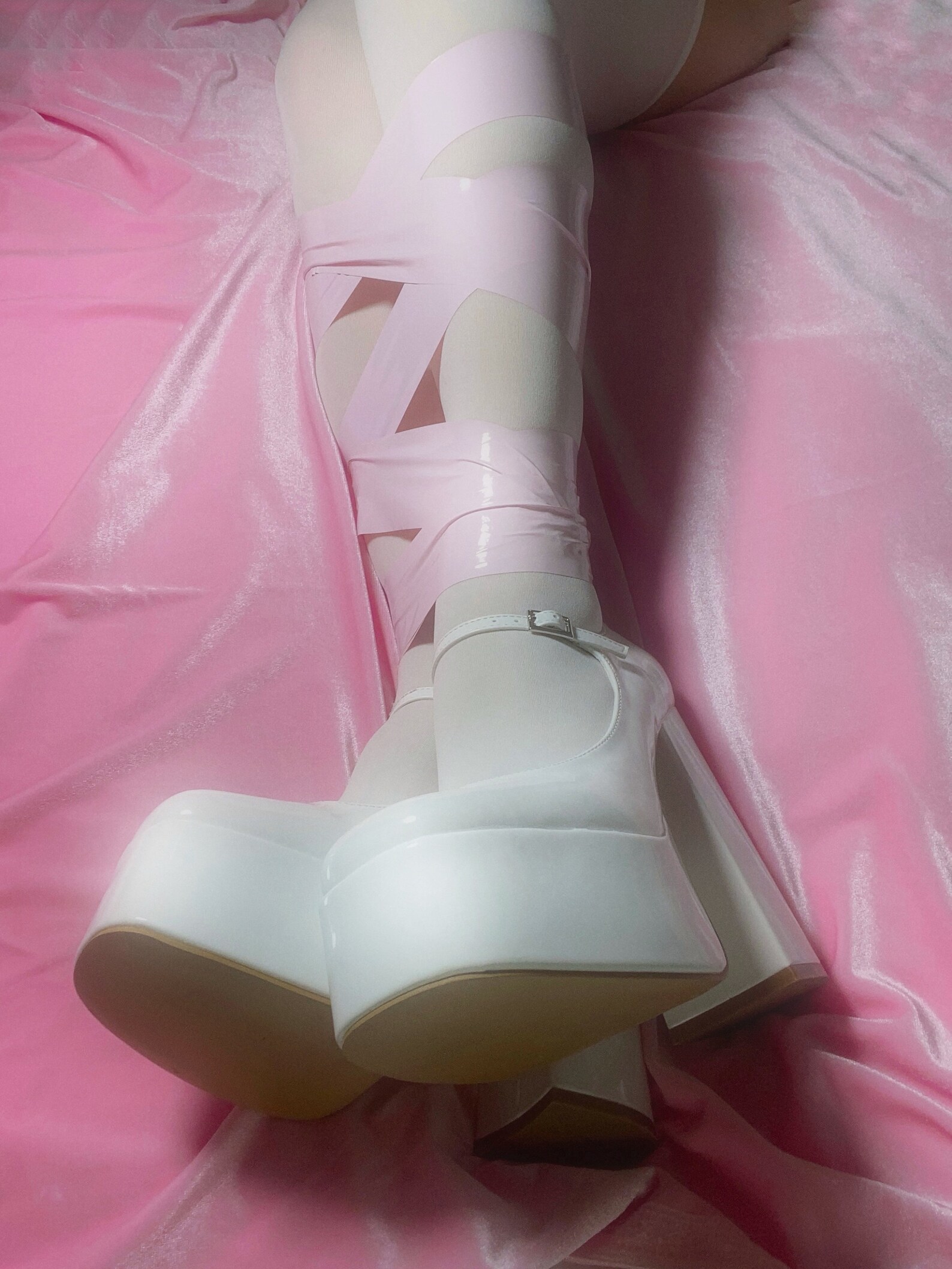 Legs wrapped in shiny pink bondage tape on pink satin bed, perfect for tie up sex or bondage restraint play.