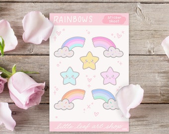以下が含まれることがあります： 上部に「RAINBOWS」の文字が入ったステッカーシート。パステルカラーの虹、星、雲にスプリンクルが施されています。「little leaf art shop」の文字が下部にあります。
