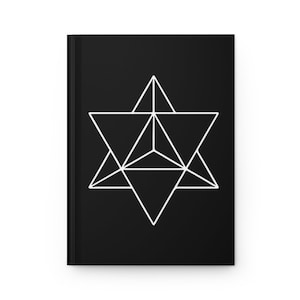 May include: Black journal with a white geometric star design on the cover. The design is a complex arrangement of interconnected triangles, creating a symmetrical pattern. The journal has a clean, minimalist aesthetic.