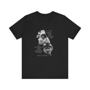 Pode incluir: Camiseta preta com uma imagem branca de um busto de homem e uma citação de Marco Aurélio que diz: "Não é a morte que um homem deve temer, mas ele deve temer nunca começar a viver."