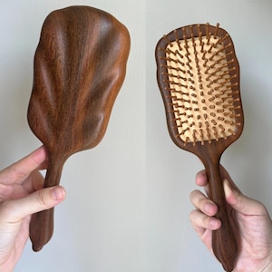 May include: Two wooden hairbrushes. One has a leaf-like shape with a handle. The other is rectangular with wooden bristles and a handle. Both are made of dark brown wood.