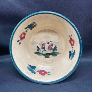 May include: A cream-colored ceramic bowl with a blue rim and a painted scene of dancing figures. The bowl features floral accents in red and green. The interior has a cracked glaze effect, adding to its vintage charm.